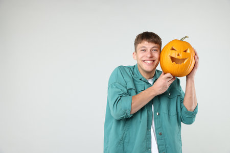 Halloween celebration. Man holding pumpkin with carved spooky face on light gray background, space for textの写真素材