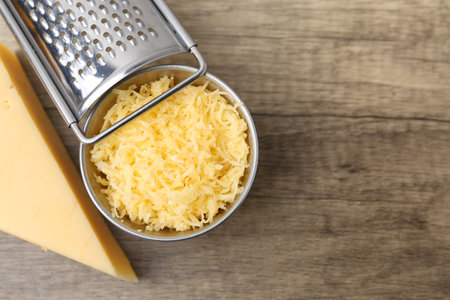 Grated and piece of cheese with grater on wooden table, flat lay. Space for textの写真素材