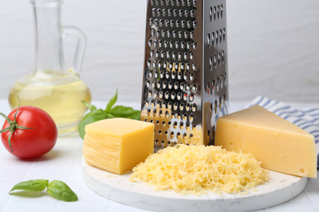 Grated cheese, grater and products on white tiled table, closeupの写真素材