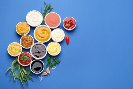 Different sauces, spices and herbs on blue background, flat lay. Space for text
