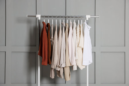 Different clothes hanging on rack near gray wall indoors