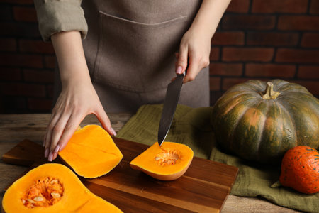 Woman cutting pumpkin at wooden table against brick wall, closeupの写真素材