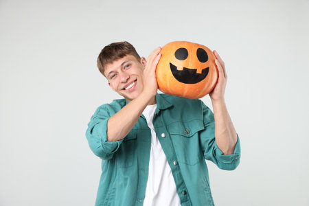 Halloween celebration. Man holding pumpkin with drawn spooky face on light gray backgroundの写真素材