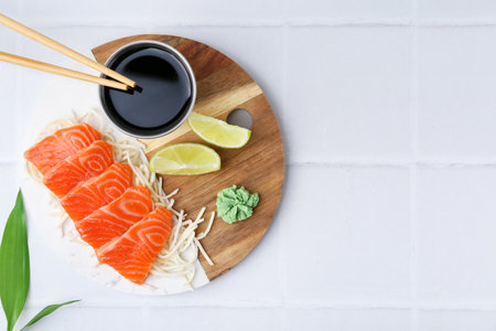 Fresh salmon sashimi with sliced radish, wasabi, lime and soy sauce on light tiled table, flat lay. Space for textの写真素材