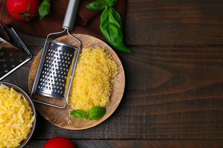 Grated cheese, graters, tomatoes and basil on wooden table, flat lay. Space for textの写真素材