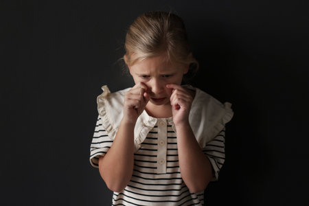 Sad little girl crying on black backgroundの写真素材