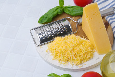 Grated cheese, grater and products on white tiled table, closeup. Space for textの写真素材