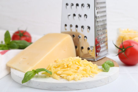 Grater, tomatoes, basil, grated and piece of cheese on white table, closeup