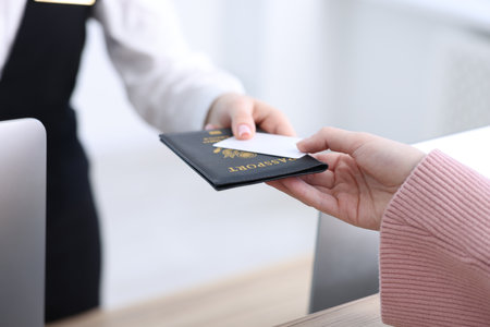 Receptionist giving passport and hotel key card to guest at reception desk indoors, closeupの写真素材