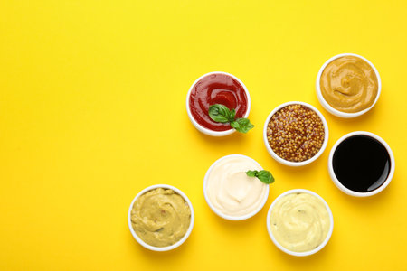 Different sauces and herbs on yellow background, flat lay. Space for textの写真素材