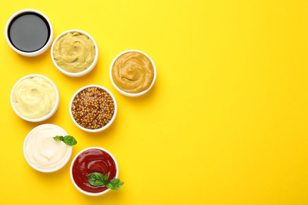 Different sauces and herbs on yellow background, flat lay. Space for text