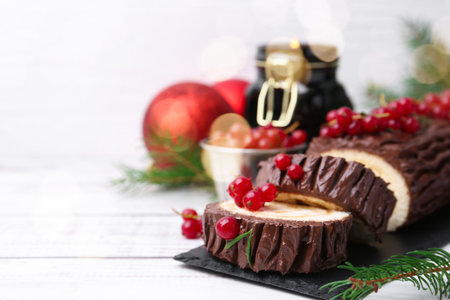 Delicious Yule log (traditional Christmas cake) with redcurrant, decor and fir tree branches on light wooden table, closeup. Space for textの写真素材