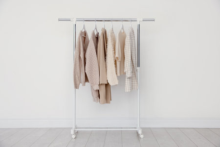 Different clothes hanging on rack near light wallの写真素材