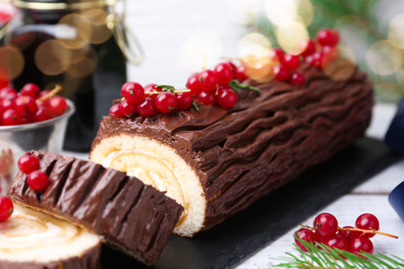 Delicious Yule log (traditional Christmas cake) with redcurrant on light table, closeupの写真素材