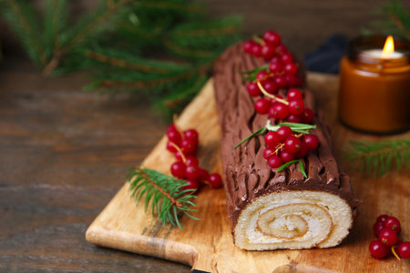 Delicious Yule log (traditional Christmas cake) with redcurrant and fir tree branches on table, closeup. Space for textの写真素材