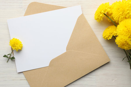 Blank card in envelope and flowers on white wooden table, flat lay. Mockup for designの写真素材