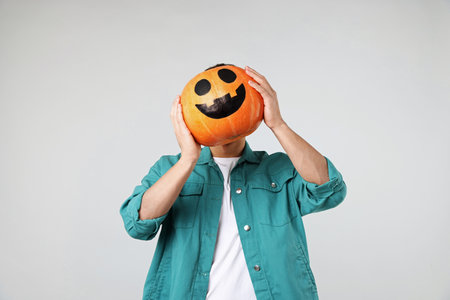 Halloween celebration. Man holding pumpkin with drawn face on light gray backgroundの写真素材