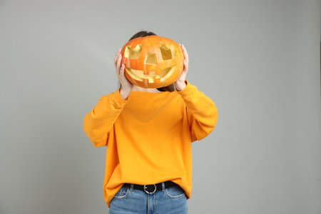 Happy Halloween. Woman hiding behind carved pumpkin on gray backgroundの写真素材