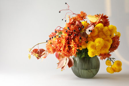 Autumn atmosphere. Vase with beautiful flowers and berries on light gray background, space for textの写真素材