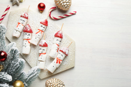 Christmas food. Funny snowmen made of marshmallows, strawberries and decor on wooden table, flat lay. Space for textの写真素材