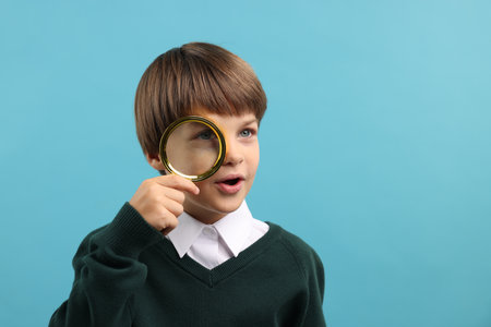 Little boy with magnifying glass on light blue background. Space for textの写真素材