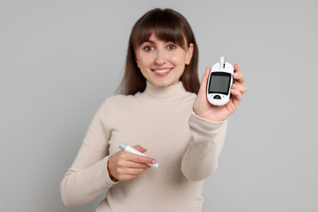 Diabetes test. Woman with lancet pen and glucometer on light gray background, selective focusの写真素材