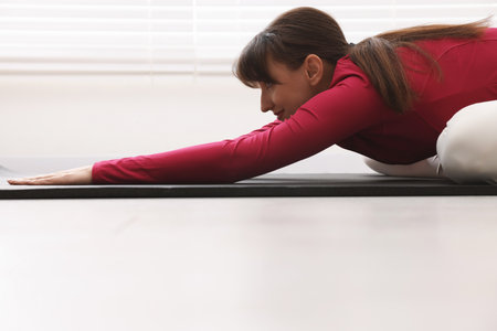 Woman in sportswear practicing yoga on mat indoorsの写真素材