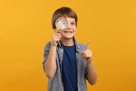 Little boy with magnifying glass on yellow backgroundの写真素材