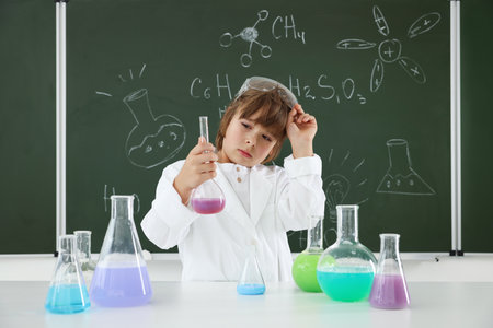 Back to school. Boy doing chemical research at desk against chalkboard with formulas indoorsの写真素材
