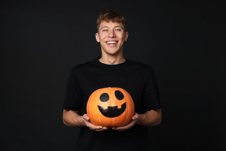 Halloween celebration. Man holding pumpkin with drawn spooky face on black backgroundの写真素材