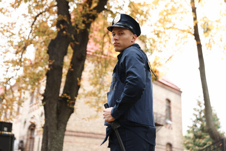 Police officer in bulletproof vest with baton at park, low angle view. Space for textの写真素材