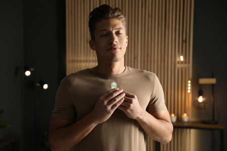 Man meditating with crystal to heal or restore his aura indoors