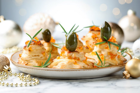 Tasty snacks with puff pastry, olives, red caviar and Christmas decor on white marble table against gray background, closeupの写真素材