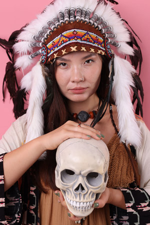 Shaman woman in native American Indian headdress with skull on pink background