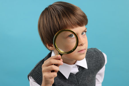 Little boy with magnifying glass on light blue backgroundの写真素材