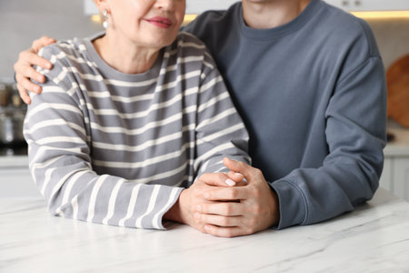 Son embracing his mother at white marble table in kitchen, closeupの写真素材