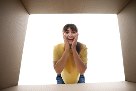 Woman looking into cardboard box against white background, view from inside package