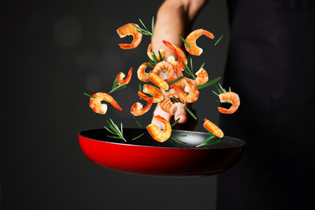 Chef tossing shrimps and rosemary in pan against black background, closeupの写真素材