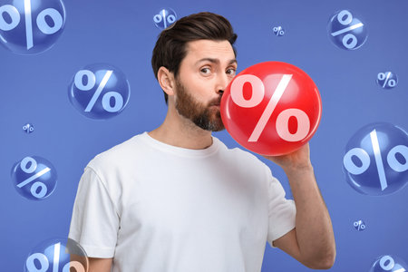 Man blowing balloon with percent sign on blue background. Discount
