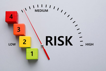 Arrow pointing at scale displaying level of risk on light gray background, top view. Cubes with...