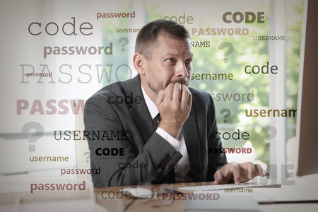 Worried man trying to remember username and password at table with computerの写真素材