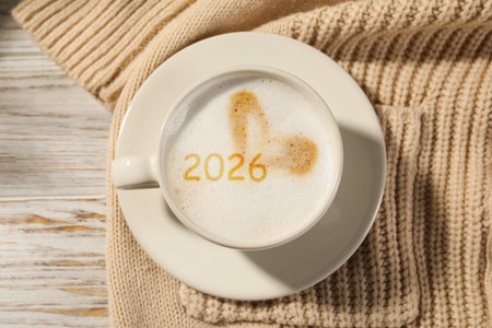 Hello New 2026 Year. Cup of coffee with numbers and knitted blanket on wooden table, top view