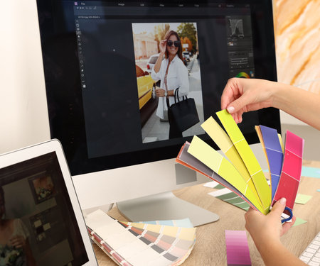 Professional retoucher with color palettes editing photo on computer and laptop at table in office, closeupの写真素材