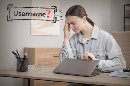 Troubled woman with laptop trying to remember password and username at tableの写真素材