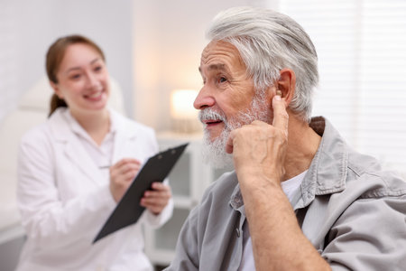 Senior man with hearing aid and doctor working in hospital, selective focusの写真素材