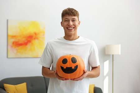 Halloween celebration. Man holding pumpkin with drawn spooky face indoorsの写真素材