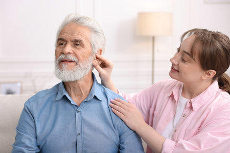 Caregiver helping senior man to put in hearing aid at homeの写真素材