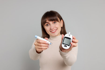 Diabetes test. Woman with lancet pen and glucometer on light gray background, selective focusの写真素材