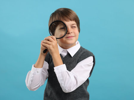 Little boy with magnifying glass on light blue backgroundの写真素材