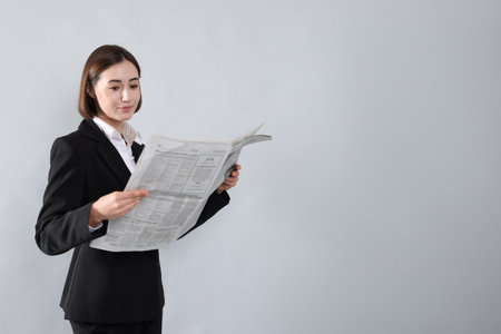 Woman in suit reading newspaper on gray background. Space for textの写真素材
